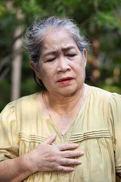 Elderly asian senior woman feels tired, flushing and sweating from excessive outdoors tropical summer heat, having breathing difficulty or shortness of breath due to prolonged dehydration
