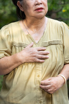 Elderly asian senior woman feels tired, sweating from excessive outdoors tropical summer heat, having breathing difficulty or shortness of breath due to prolonged dehydration, hand closeup shot