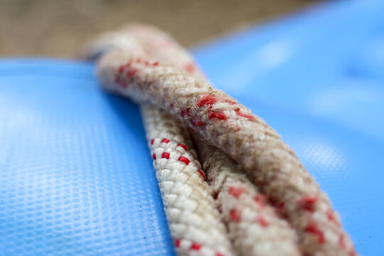White braided rope with red tracers resting on blue textured plastic surface, close up macro showing fiber detail and worn texture conveying tactile and practical use