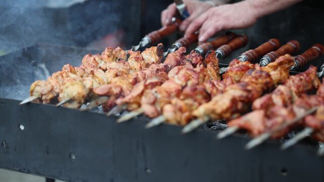 Cook grilling meat skewers on coal brazier. Professional chef preparing barbecue pork shashlik over open fire. Culinary process of outdoor food preparation event.