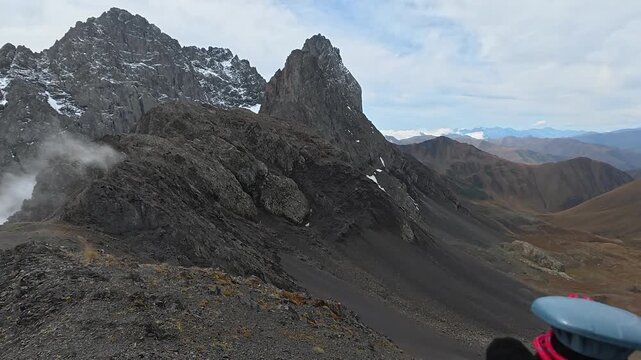 4K Chest-mounted POV of a hiker looking toward the jagged rock spires of Chaukhi Massif with clouds drifting below, Kazbegi, Georgia.