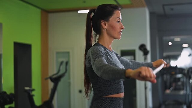 A person performs an exercise to strengthen arm muscles using controlled movements in a gym. The action takes place indoors with gym equipment visible in the background