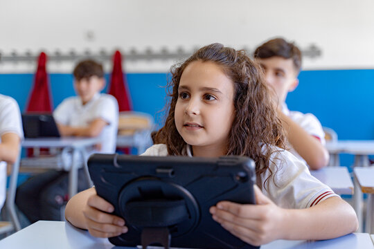 Young female student engaging with education technology, holding a device during a modern lesson in a school classroom