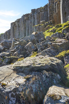 Rugged rocky terrain with moss-covered boulders and towering basalt cliffs under a clear blue sky,Gerduberg cliffs,Iceland