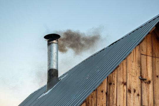 Dark smoke billowing from a metal chimney on a wooden roof