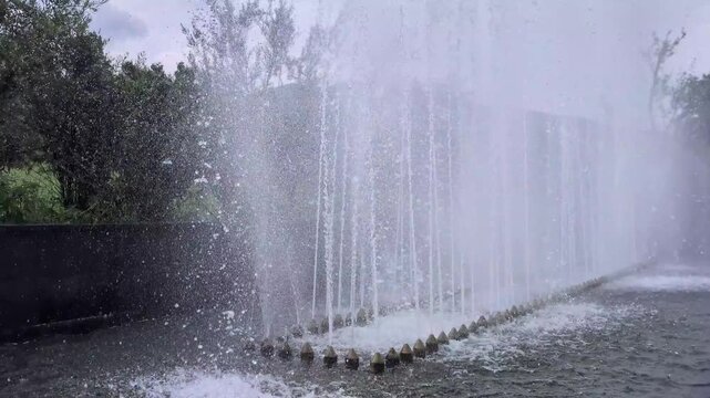 Continuous row of nozzles spraying powerful jets of water upwards in a modern fountain, creating a beautiful and refreshing wall of splashing liquid and mist in an urban park