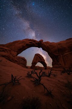 Milky way galaxy rising above natural stone arches in desert at night with astronomy landscape outdoors sandstone