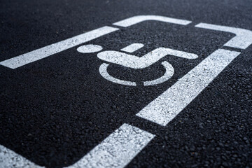 Obraz premium White painted disabled parking space symbol on dark asphalt surface close up.