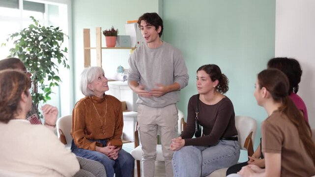 European guy stands in front of a group of people and talks against the background of the interior in the office. Guy communicates with a psychological support group . High quality 4k footage