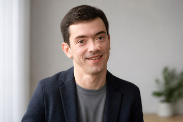 Fototapeta premium A smiling man in a dark blazer is posing indoors against a light background.