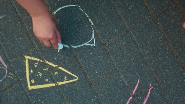 Woman hand drawing hopscotch with colorful chalk on stone sidewalk tiles. Playful outdoor activity for kid. Artistic decoration of asphalt path in summer. Creative childhood hobby.