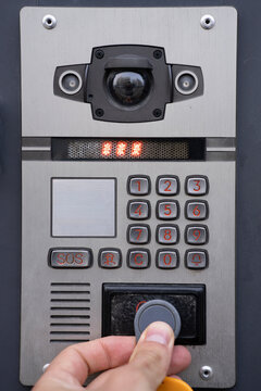 Close up view of a hand applying RFID key fob to an outdoor intercom reader panel with digital keypad and camera for entrance access.