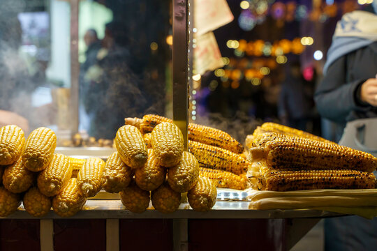 grilled corn cooking at night market with steam and warm inviting atmosphere close-up yellow brown husks metal stall food street natural light clean background copy space editorial resource.