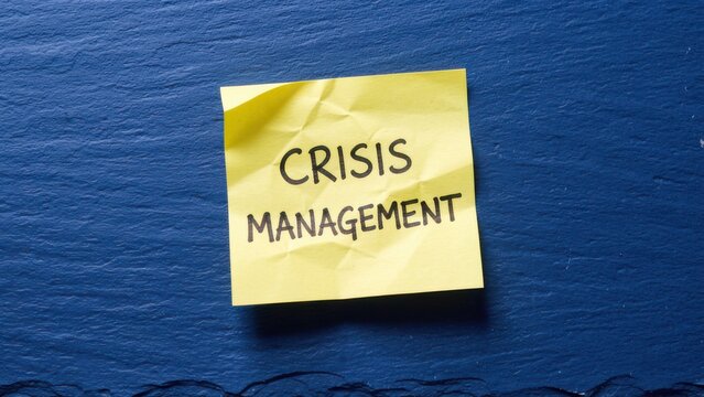 overhead shot of yellow sticky note with crisis management text on deep blue slate for business planning concept
