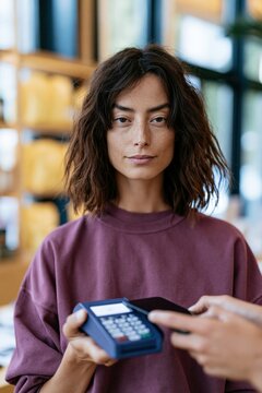Young woman holding a card reader while processing contactless payment at a cozy cafe counter for checkout banner and retail marketing use