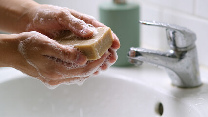Fototapeta premium Person Washing Hands With Natural Bar Soap at the white sink For Proper Daily Hygiene And Cleanliness