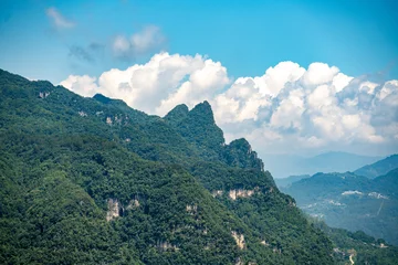 The lush green mountains rise above the Three Gorges Reservoir near Yichang in China under a bright blue sky with white clouds during the summer season © AS_SleepingPanda