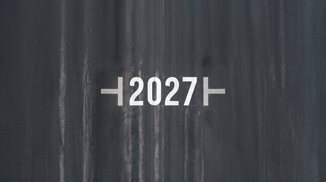 Large white number 2027 painted clearly on the dark gray asphalt surface of an airport runway captured from a high angle drone perspective view.