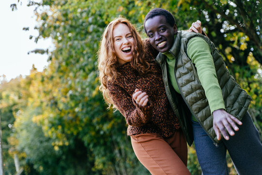 Joyful multiracial female friends laughing and embracing during autumn orchard adventure