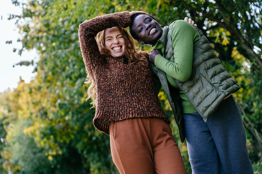 Playful multiracial female friends laughing together during joyful autumn walk in countryside