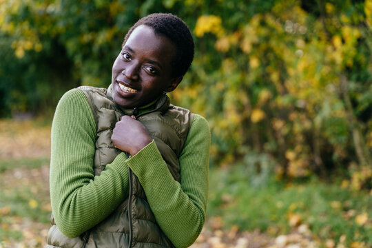 Cheerful Black woman smiling warmly in cozy green sweater during relaxed autumn walk outdoors