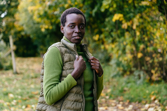 Confident Black woman in green sweater and quilted vest posing outdoors in autumn nature