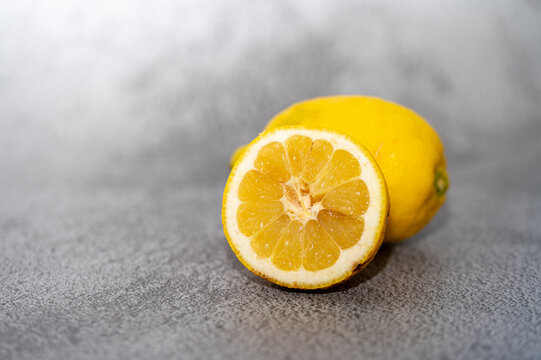 Fresh lemon and a cut lemon half on a grey background.Close-up of a whole ripe yellow lemon alongside a fresh juicy lemon half, showcasing the textured pulp and rind.