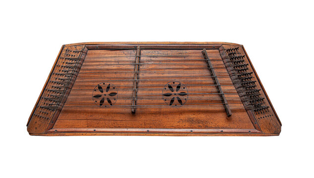 An antique wooden dulcimer with intricate soundhole carvings is isolated on a clean white background.