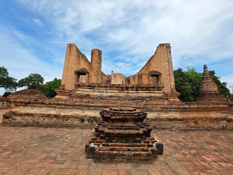 Ancient Ruins in Thailand: Sun-drenched ancient ruins in Thailand, featuring weathered brick structures and pagodas, stand testament to a bygone era under a clear blue sky dotted with fluffy clouds.