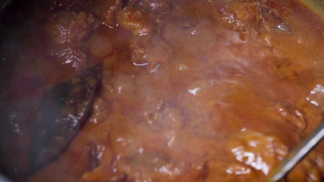 Spicy Indian mutton curry simmering on the stove in a traditional home kitchen.