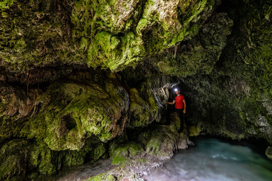 Explorer with headlamp walks through a mossy cave beside a stream, embodying outdoor adventure in Sorna river, Rovereto, Vallagarina, Brentonico plateau, Trentino, Italy.