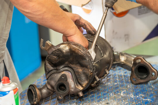 Mechanic repairing a car catalytic converter or DPF exhaust system with a pneumatic chisel. Automotive garage workshop, professional vehicle maintenance, and metal parts recycling concept.