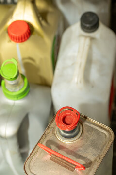 A high-angle, close-up shot of various plastic fuel jerrycans with colorful caps alongside an old metal canister stored in a garage. Ideal for concepts related to automotive fluids, chemical storage, 