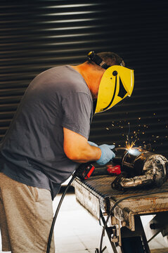 Professional welder or craftsman working in a workshop with bright sparks flying. Industrial manufacturing, metalwork fabrication, and protective safety helmet concept.