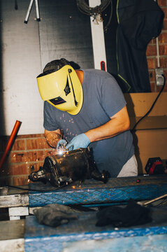 Close-up of a mechanic using a welding torch to repair a metal car exhaust part, probably a catalytic converter or diesel particulate filter (DPF). Bright sparks fly during the metal welding process o
