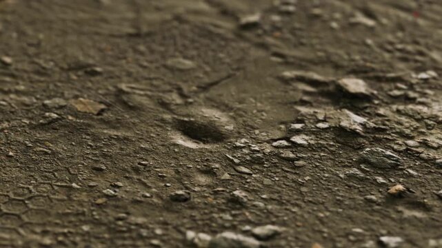 A close up of ground showing texture with various small rocks and noticeable patterns. The surface appears dry and rugged, reflecting natural elements and conditions.