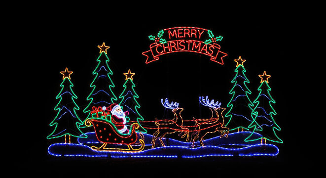 A vibrant light-up Christmas display features a festive scene with illuminated trees, Santa Claus, and reindeer. The design includes a "Merry Christmas" banner and a snowy landscape.