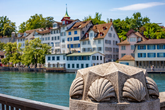 Close up of a decorative stone shell carving on a bridge railing with a blurred background of scenic traditional colorful waterfront buildings and Limmat river in Zurich on a sunny summer day