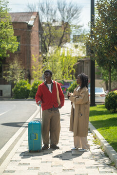 Stylish african american married couple man and woman travelers standing on street waiting for taxi, thoughtful black male and female tourists on holiday trip in new city, looking around town.
