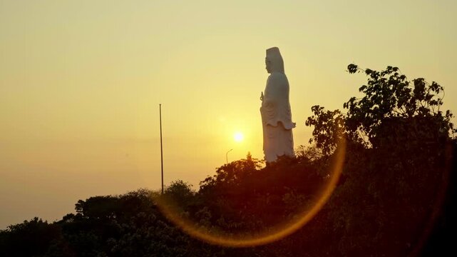 Artistic shot of the Lady Buddha statue at sunset, enveloped by a vibrant orange halo, creating a spiritual and dramatic silhouette in Da Nang, Vietnam.