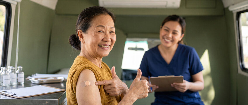 Smiling senior Asian woman showing vaccination bandage and thumbs up in mobile clinic, National Immunization Awareness Month concept