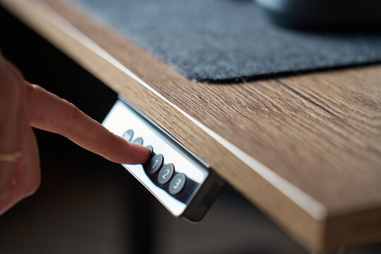 Finger pressing control button on adjustable wooden desk to change desk height
