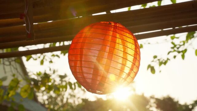 Close-up of a vibrant red Vietnamese lantern glowing in front of a majestic sunset over a traditional temple, evoking peace and cultural ambiance.