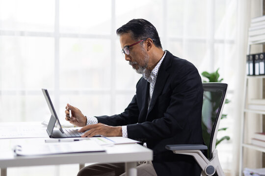 Asian businessman working on digital tablet at office desk.