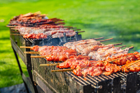 Rows of chicken skewers cooking on a long barbecue grill outdoors on a sunny day