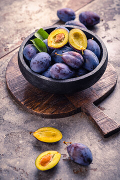 Fresh ripe plums in a rustic bowl on a wooden board, a healthy fruit snack