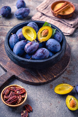 Obraz premium Fresh ripe plums in a rustic bowl on a wooden board, a healthy fruit snack