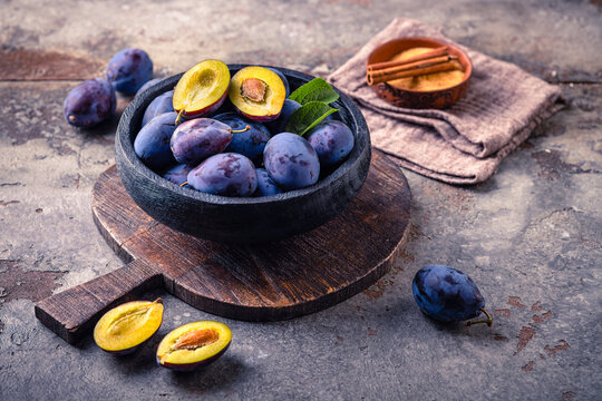 Fresh ripe plums in a rustic bowl on a wooden board, a healthy fruit snack