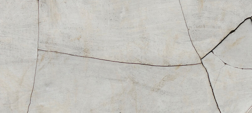 A close-up photo of a severely cracked gray cement plaster surface.