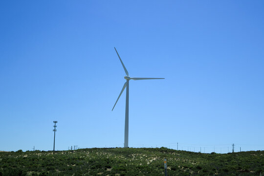 A tall white wind turbine generates renewable energy on a green hillside under a sunny sky along Interstate-8 near city of Campo in southern California